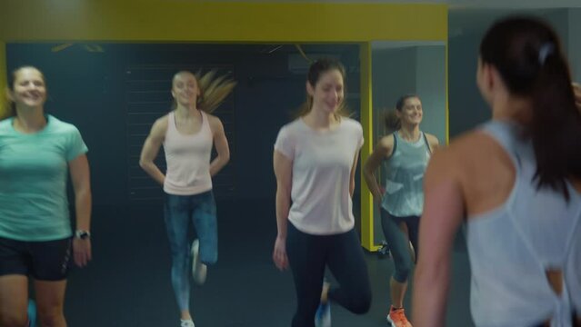Small group of women doing warm-up exercises in the fitness class, guided by a female professional tabata instructor, handheld shot.