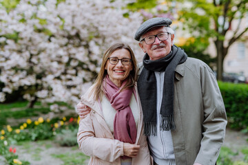 Adult daughter hugging her senior father outdoors in park on spring day.