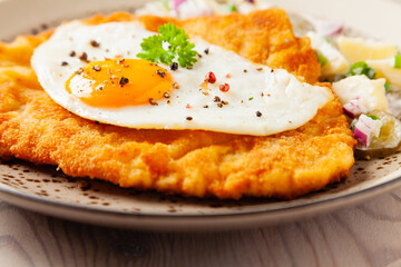 Viennese pork schnitzel with a fried egg. Served on potato salad. Natural wooden planks in the background.