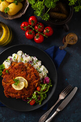 Classic, traditional Viennese sirloin schnitzel. Served on potato salad. Breaded. Dark background.