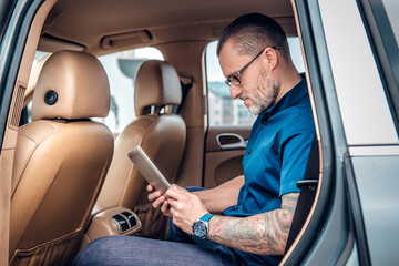 Fototapeta Portrait of tattooed serious old man executive with tablet sitting inside of car. obraz
