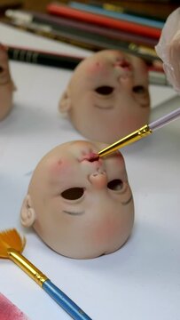 Making dolls. Master painter carefully paints lips of blank for doll with thin brush.