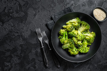 Boiled broccoli with spices in a plate. Black background. Top view. Copy space