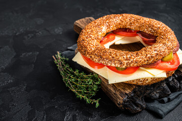 Simit bagel sandwich with lettuce, tomato, yellow cheese and ham. Black background. Top view. Copy space
