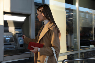 Young woman using cash machine for money withdrawal outdoors