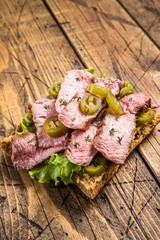 Griiled Steak sandwich with sliced beef, rocket and vegetables on bread. Wooden background. Top view
