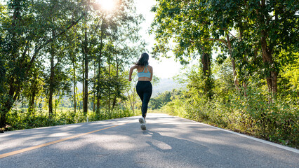 Slender beautiful girl in sportswear jogging along the road on a bright morning, girl running in the autumn forest. Back view. On the road. Outdoor shooting.
