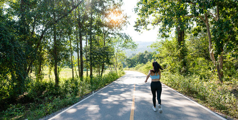 Slender beautiful girl in sportswear jogging along the road on a bright morning, girl running in the autumn forest. Back view. On the road. Outdoor shooting.