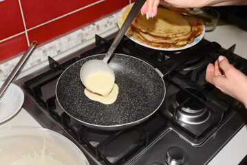 Woman pouring crepe batter onto frying pan in kitchen, closeup