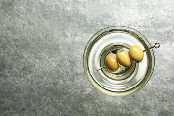 Martini cocktail with olives on grey table, top view. Space for text