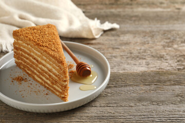 Slice of delicious layered honey cake served on wooden table. Space for text