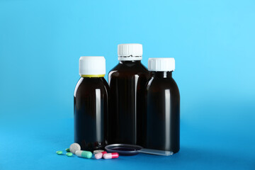Bottles of cough syrup, dosing spoon and pills on light blue background