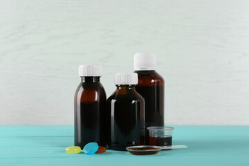 Bottles, spoon and measuring cup with cough syrup near lozenges on turquoise wooden table