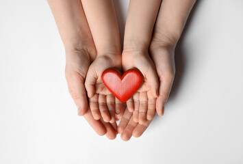 Woman and kid holding red heart in hands on white background, top view