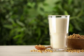 Glass with fresh soy milk and grains on white wooden table against blurred background. Space for...
