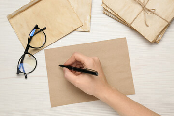 Woman writing letter at white wooden table, top view