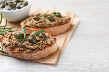 Slices of bread with delicious pate, capers and rosemary on white wooden table, closeup. Space for text