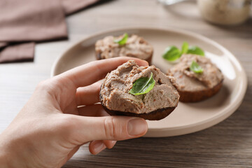 Woman taking slice of bread with delicious pate and basil from plate at wooden table, closeup