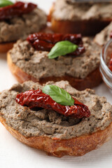 Slices of bread with delicious pate, sun dried tomatoes and basil on napkin, closeup