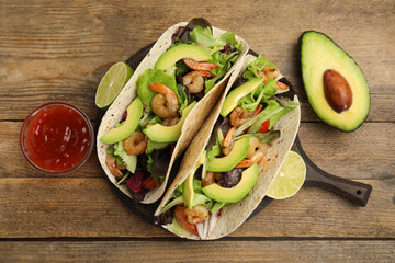 Delicious tacos with shrimps, avocado and sauce on wooden table, flat lay