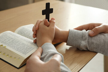 Boy and his godparent praying together at wooden table, closeup