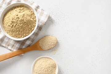 Sesame flour in bowl and white sesame seeds in wooden spoon on white background. View from above. Copy space. Good vegan source of protein, minerals, natural antioxidants and vitamins.