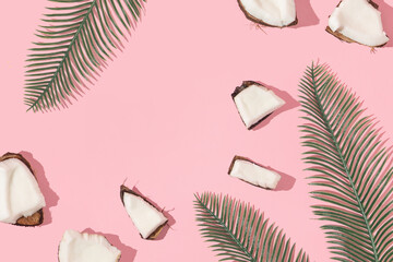 Summer creative layout with coconut pieces and palm leaves on pastel pink background. 80s or 90s...