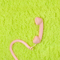 Pastel pink retro telephone handset on neon  green fluffy shaggy rug background. Vintage aesthetic...