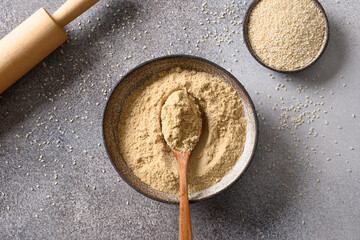 Sesame flour in bowl and white sesame seeds on gray background for cooking gluten free dessert....