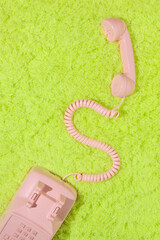 Pastel pink retro telephone with handset off handset on neon  green fluffy shaggy rug background....