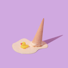 Summer creative layout with melting ice cream cone upside down and rubber duck toy on pastel purple...