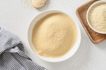 Sesame flour in bowl and organic sesame seeds on white background for cooking gluten free dessert. View from above.