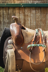 Beautiful leather saddle in the West style. Horse equipment against the background of a wooden paddock fence