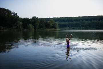 Active senior woman swimmer standing and stretching outdoors in lake.