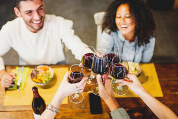 Hands toasting red wine glass and friends having fun cheering at winetasting experience, young...