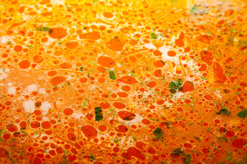 Surface of vegetable soup with drops of fat and herbs.