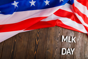 the word MLK day laid with silver metal letters on wooden surface with crumpled USA flag at upper...