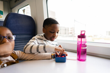 Siblings sitting on train and eating snacks