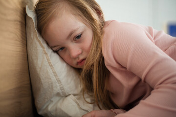Fototapeta premium Sad little girl with Down syndrome lying on bed at home.