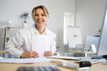 Pleasant business woman with paper sitting at the workplace - obrazy, fototapety, plakaty