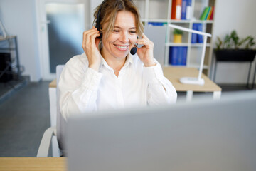 Laughing businesswoman wearing headset talking to caller in customer services department