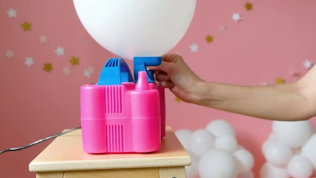 Woman decorator inflates baloons with air compressor on pink photo zone