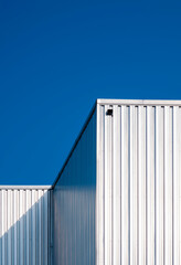 Fototapeta na wymiar Sunlight on surface of corrugated steel wall of warehouse building against blue clear sky background in vertical frame