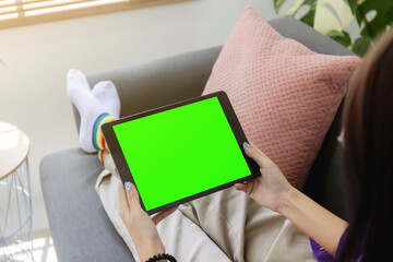 Over shoulder Girl using tablet computer on sofa in living room with blank green screen, Work from home concept.