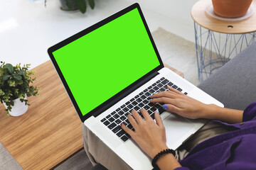 Girl using laptop computer on sofa in living room with blank green screen, Work from home concept.