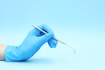 A hand in a blue glove holds a dental instrument. Close-up on a blue background. Place to copy. Medicine, dentistry