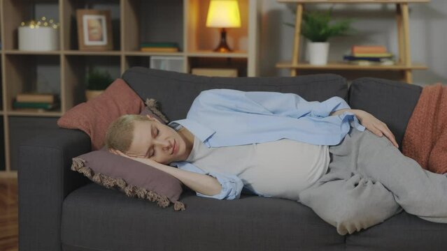 Caucasian pregnant woman enjoying sweet dreams in modern living room. Tired expectant mother napping on comfortable couch after hard day.
