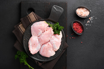 Raw chicken thigh fillet without skin with herbs and spices on black background. Farm poultry meat. Top view with copy space. Mock up. - obrazy, fototapety, plakaty