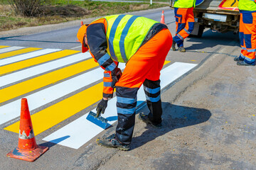 A road worker paints, repairs a pedestrian crossing on an asphalt surface on a city street.
