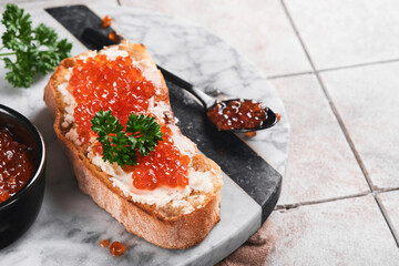Red caviar sandwiches. Salmon red caviar in bowl and sandwiches on marble plate on old gray cracked tile table background. Top view. Copy space. - obrazy, fototapety, plakaty